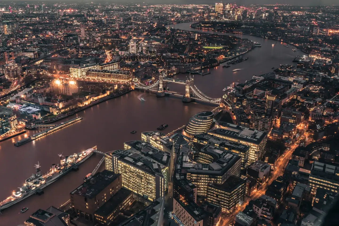 Aerial view of London at night showing the River Thames with illuminated bridges and the city's skyline with modern and historic buildings